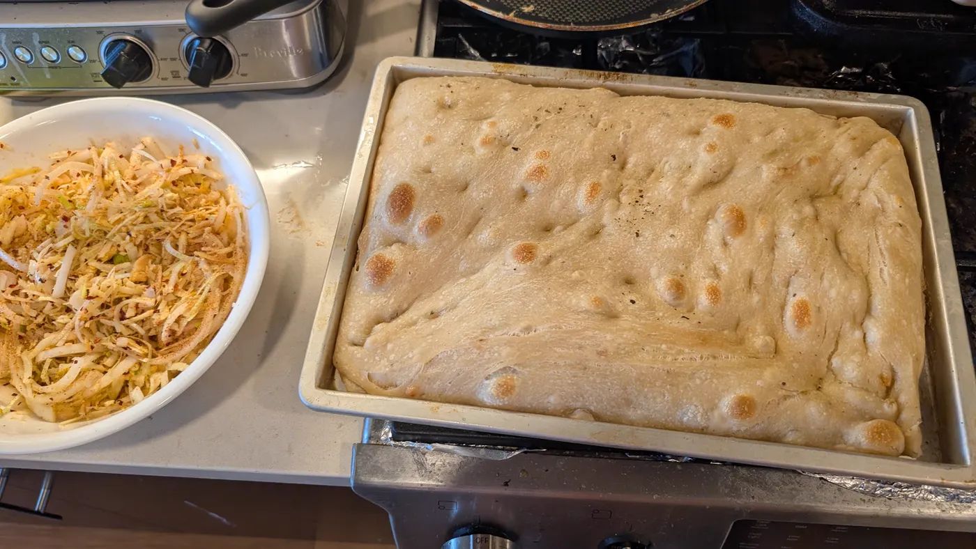 Proofed dough in an oiled pan, with a bowl of onions and cheese beside it